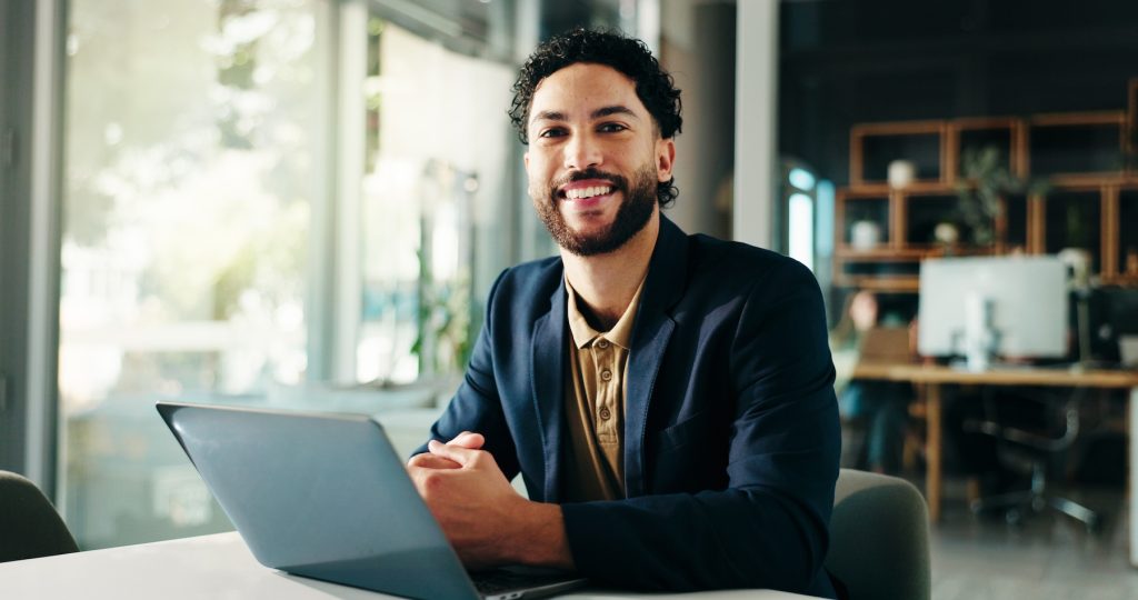 Male title insurance agent smiling, sitting with laptop
