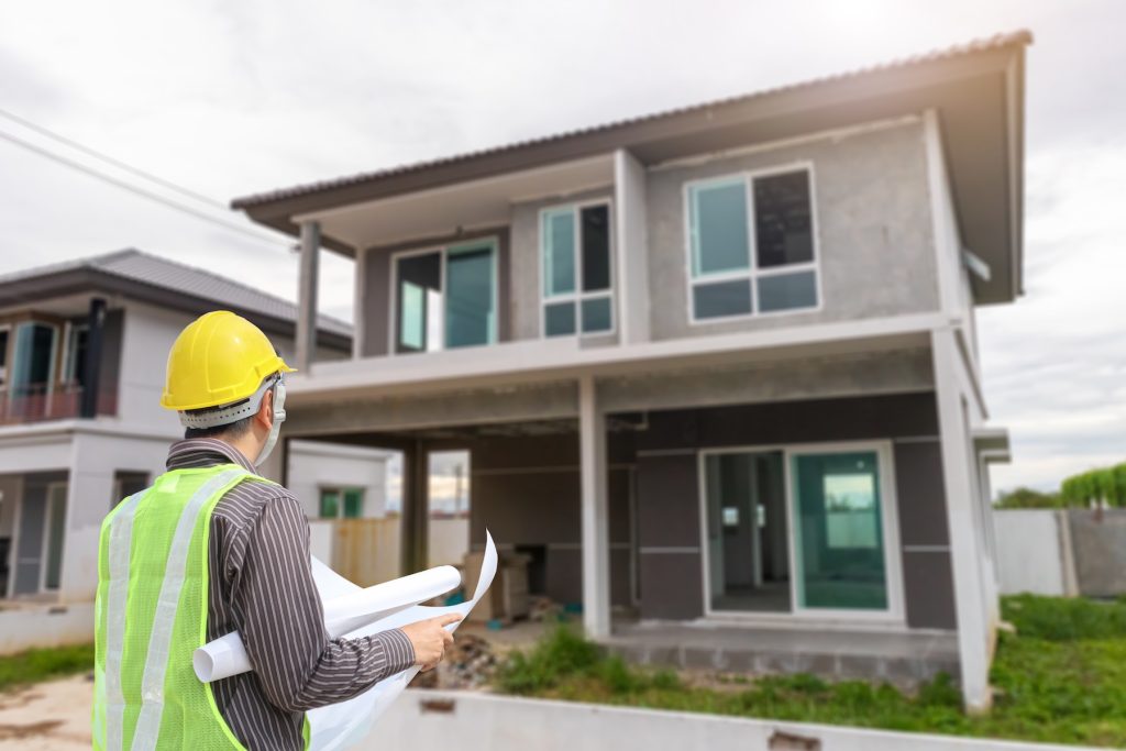 Male home inspector in hard hat standing in front of gray house